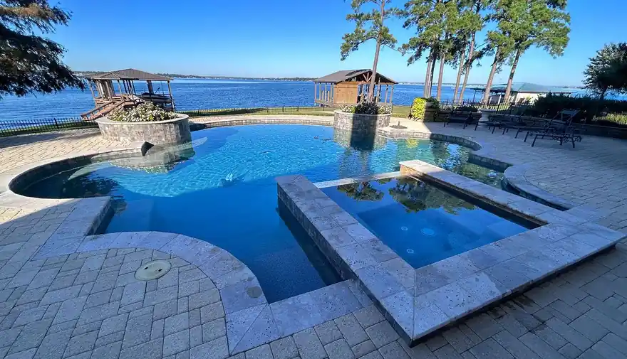 Lakefront pool and raised spa on a paver deck in bright sun
