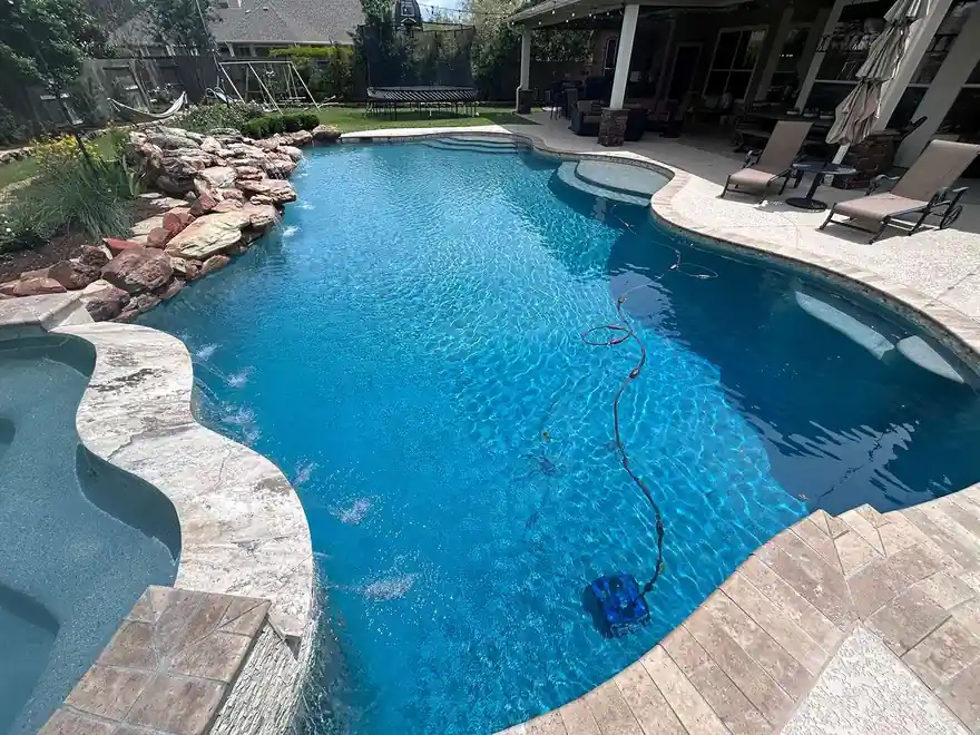 Freeform pool with a rock waterfall and an automatic cleaner on the floor