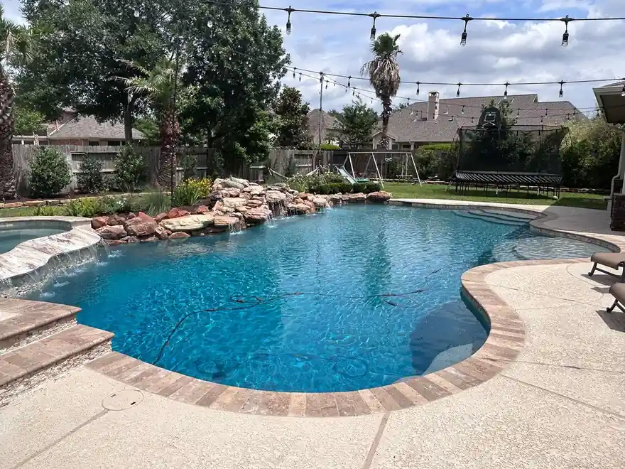 Freeform pool edged with boulders under string lights