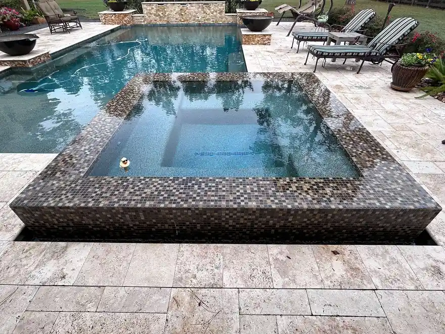 Raised spa wrapped in mosaic tile beside a travertine deck