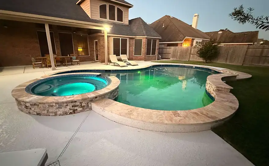 Pool and spa at dusk lit by LED lights, the house glowing behind