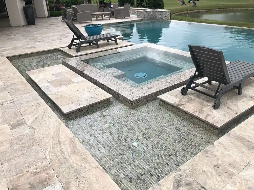 Travertine spa edge and chaise lounges beside the pool