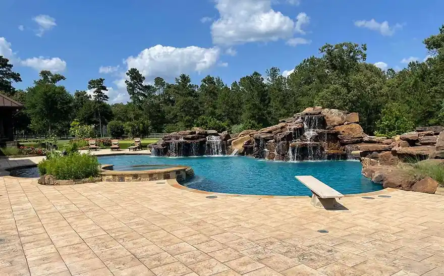Stamped concrete deck around a pool with a rock waterfall and diving board